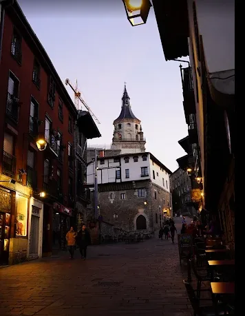 Calle del Casco Viejo de Vitoria-Gasteiz al anochecer, con una torre de iglesia al fondo.
