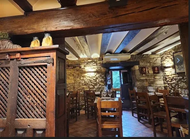 Comedor de la taberna con vigas de madera, paredes de piedra y un armario antiguo de madera con celosía.