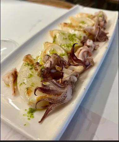 Txipirón a la plancha con aceite de perejil en fuente blanca.